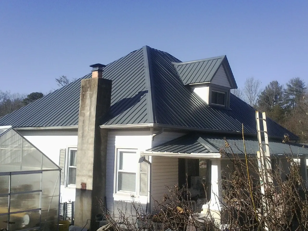 Dark blue standing seam metal roof on a white farmhouse with dormer — Slate & Tile Roof Repair by Roofing Brothers in Galena Park