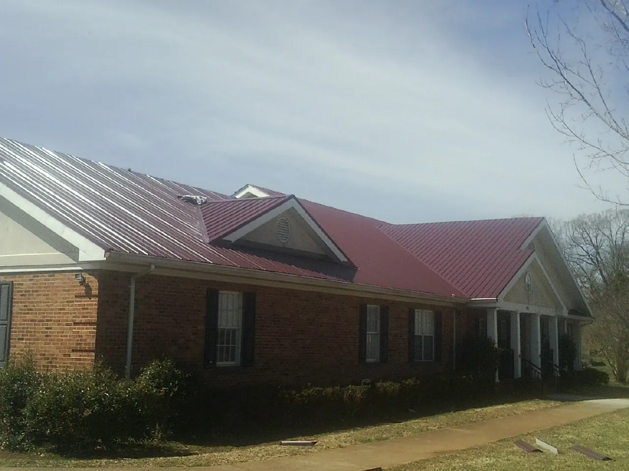 Red metal roof with gabled entries on a long brick building, from a Hail Damage Roof Repair job in Galena Park