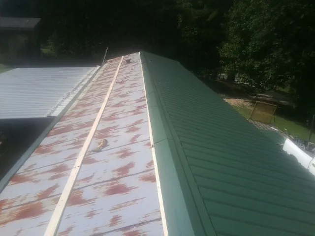 Old rusted panels beside newly installed green metal roofing — Wind Damage Roof Repair by Roofing Brothers in Galena Park