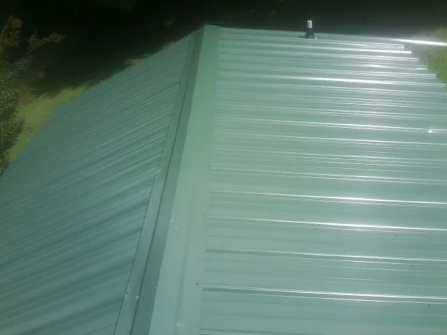 New green metal panels meeting at the ridge of a roof — Flat Roof Repair work by our crew in Galena Park