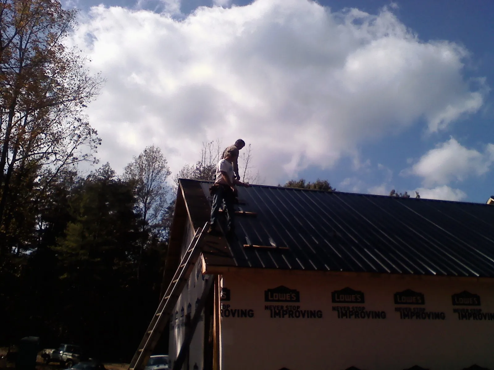 Roofer fastening dark metal panels high against a cloudy sky, from a Roof Inspection job in Galena Park