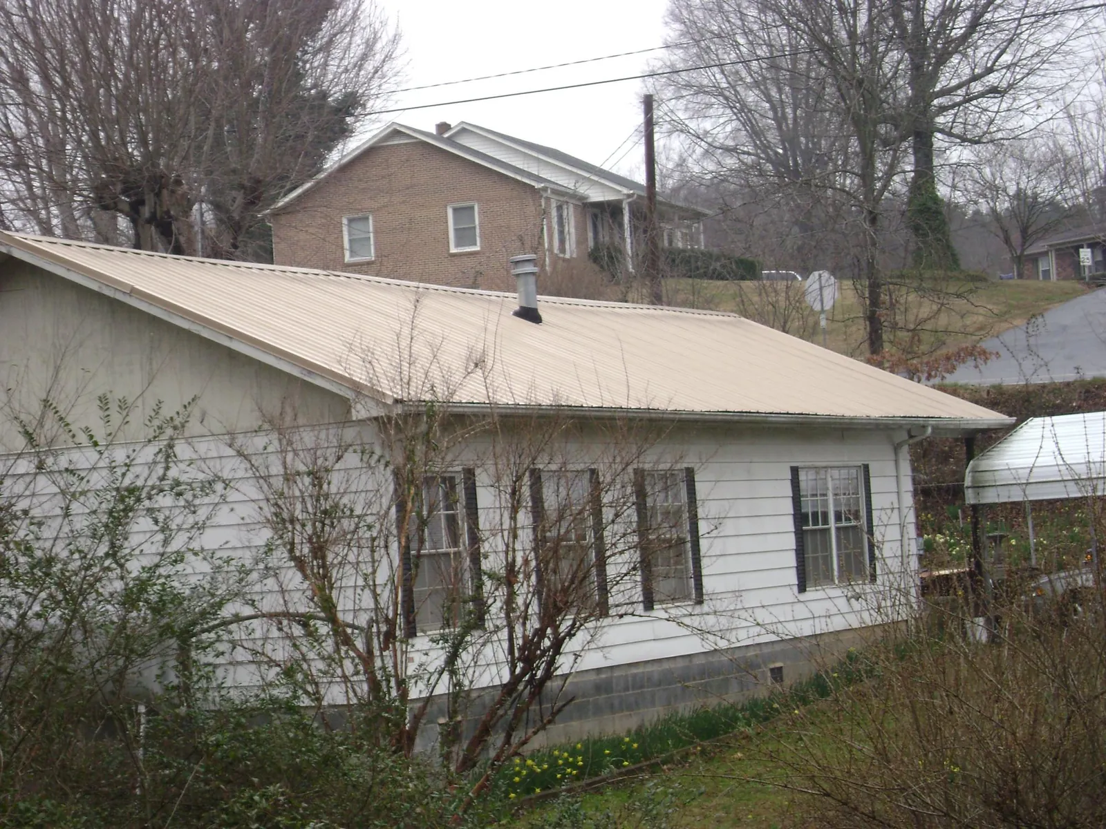 Tan metal roof on a white sided house set into a hillside — Commercial Roofing by Roofing Brothers in Galena Park